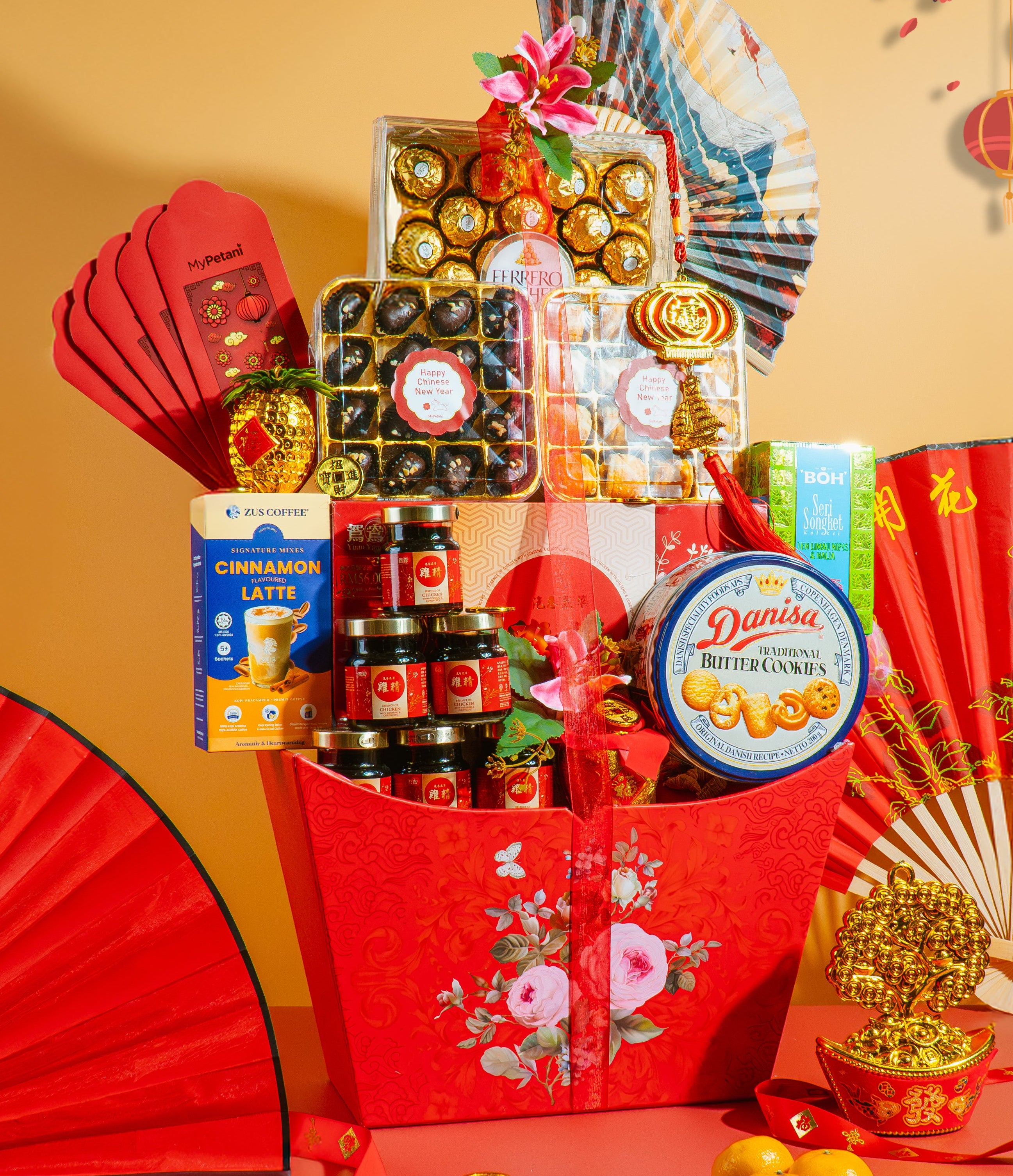 Chinese New Year 2026 gift hamper with various items including a CNY cookies, essence chicken, ferrero rocher premium chocolates, candies, and a box of tea on a peach background.