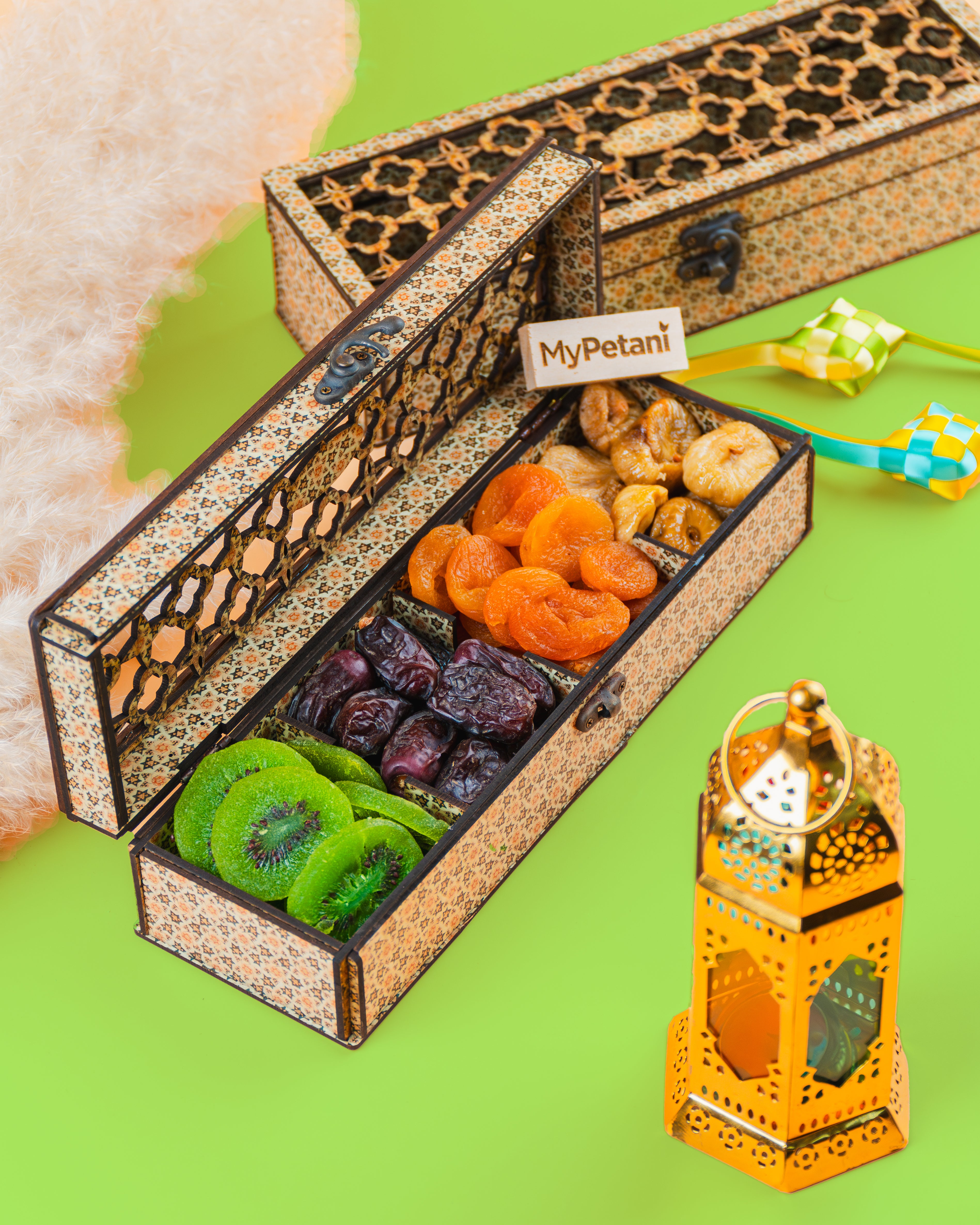 A beautifully packaged gift box containing an assortment of dried fruits including apricots, figs, and kiwis, with a decorative lantern beside it.