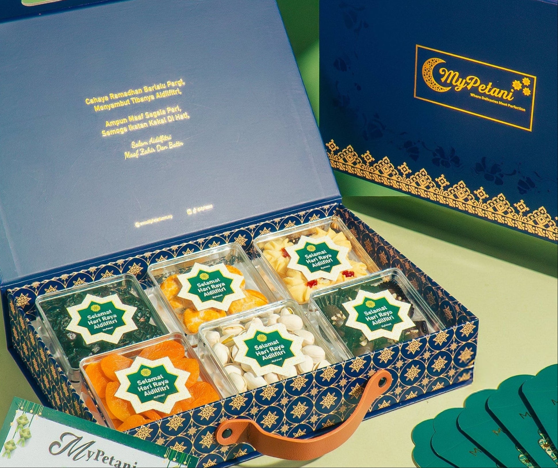 Elegant blue gift box with Raya cookies, cards, and decorative elements on a green background