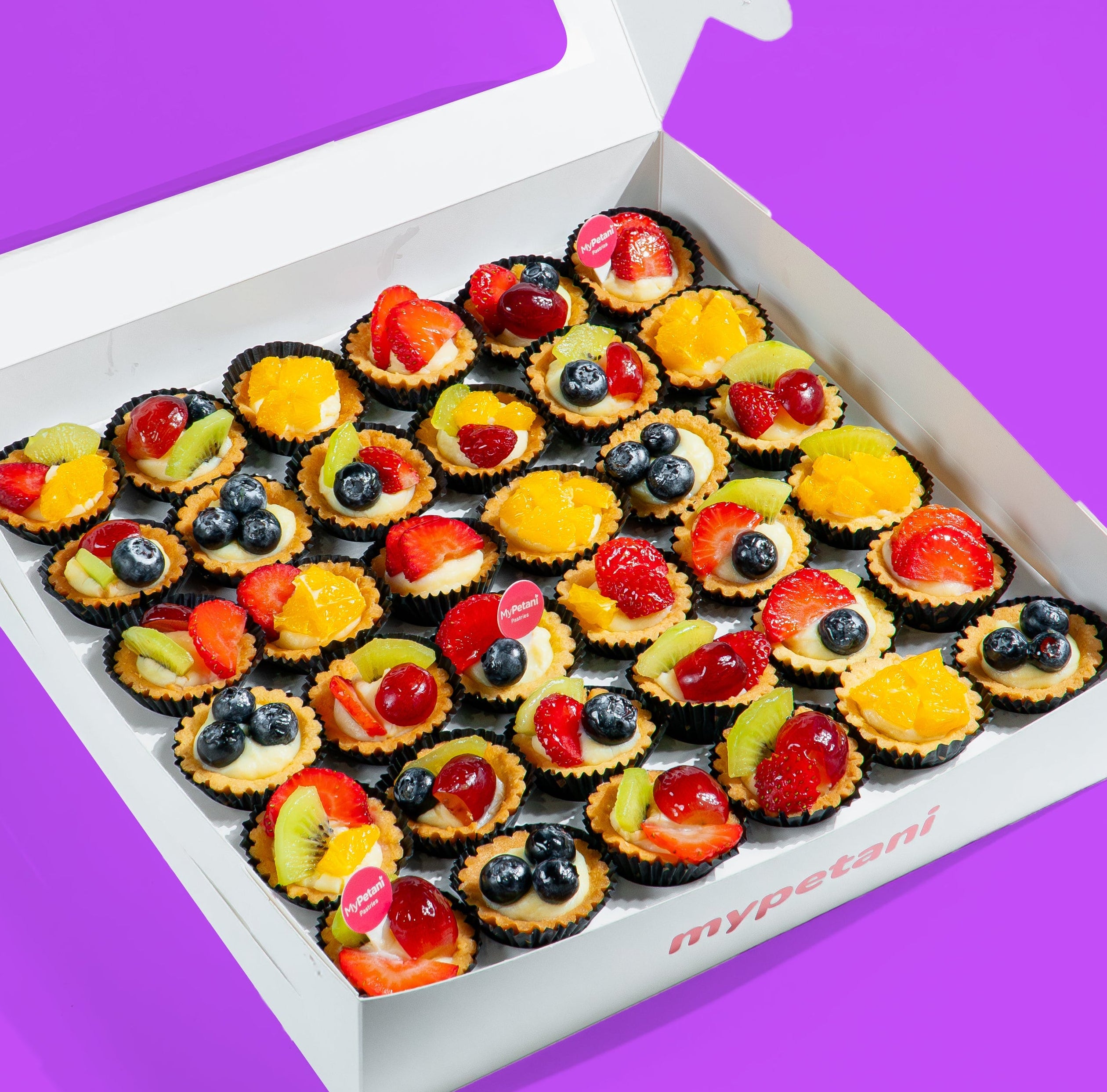 Box of assorted fruit tarts on a purple background