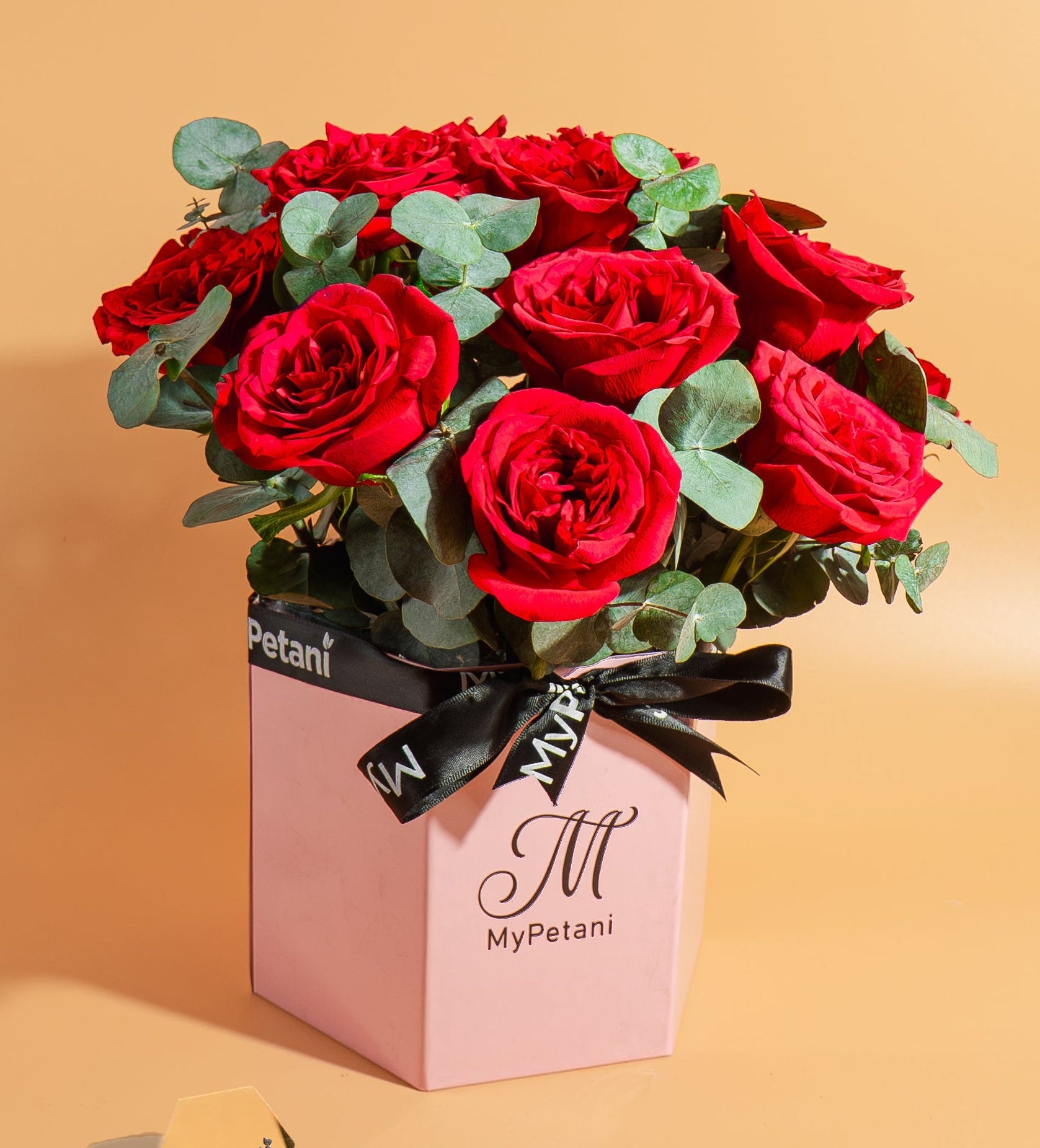Bouquet of red roses in a pink box with 'MyPetani' branding on a beige background