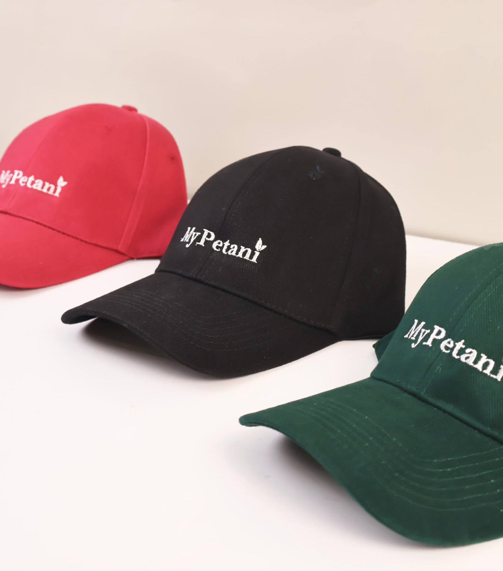 Three caps in red, black, and green with 'MyPetani' logo on a light background