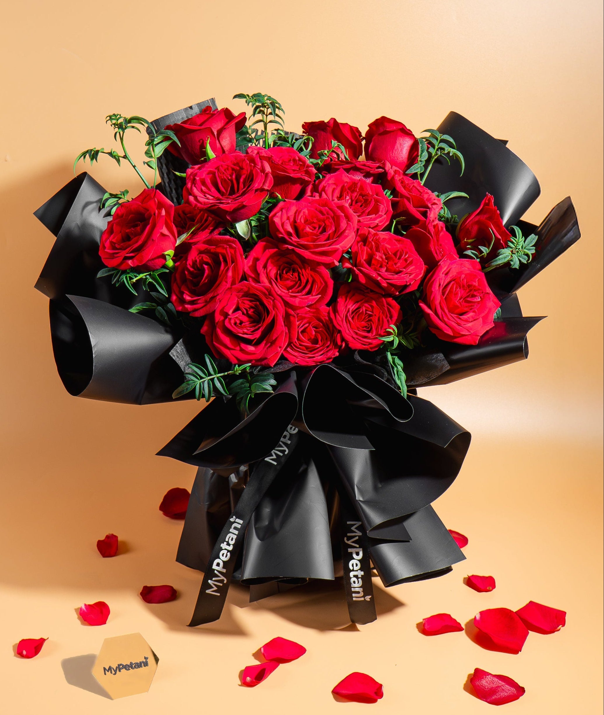 Bouquet of red roses wrapped in black paper with petals scattered on a beige background