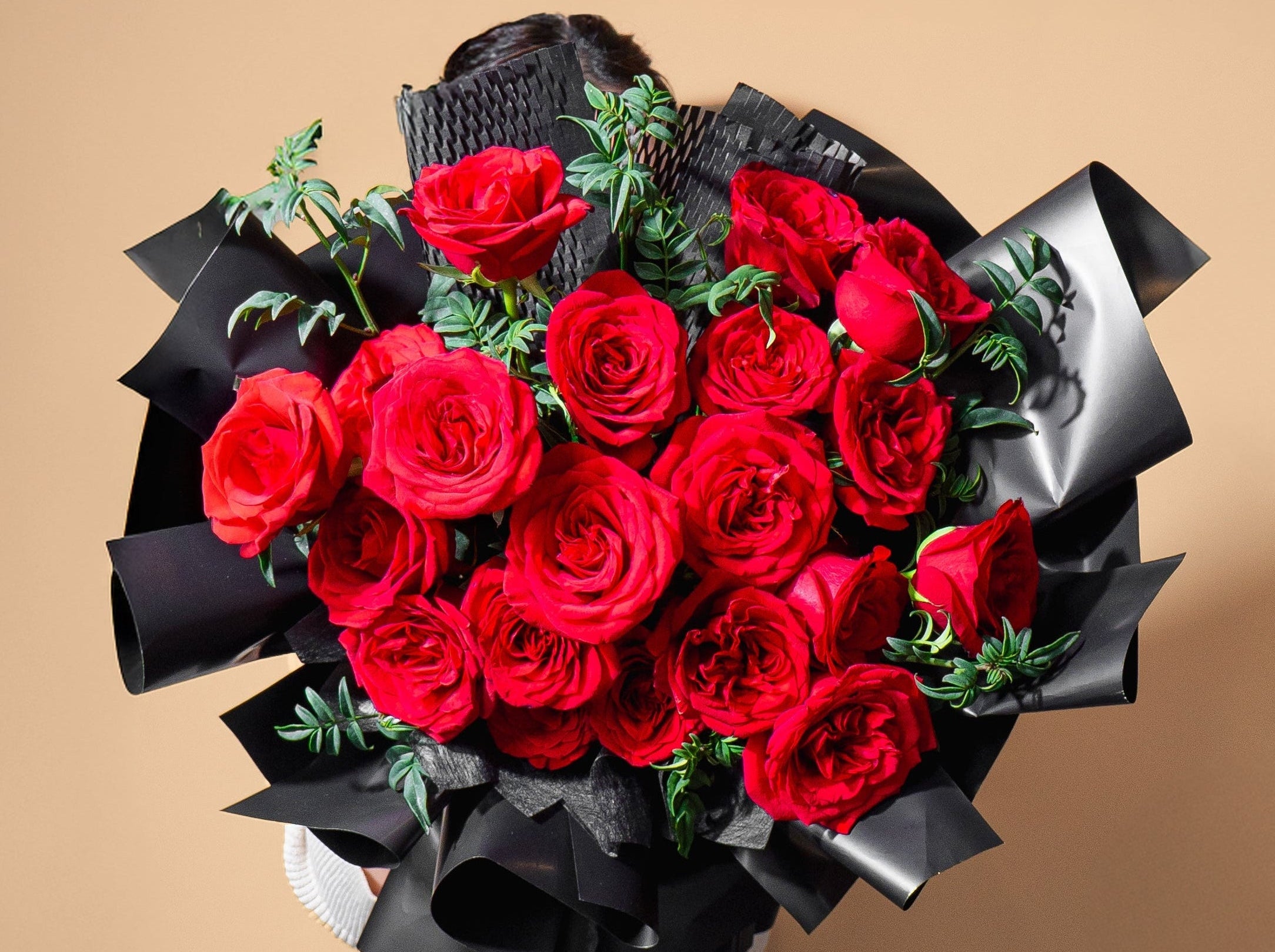 Bouquet of red roses wrapped in black paper held by a person against a beige background