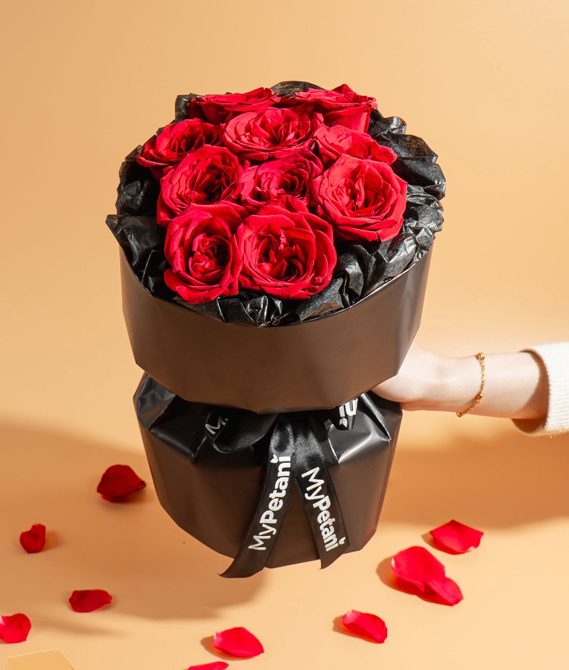 Black box with red roses held by a hand on a beige background