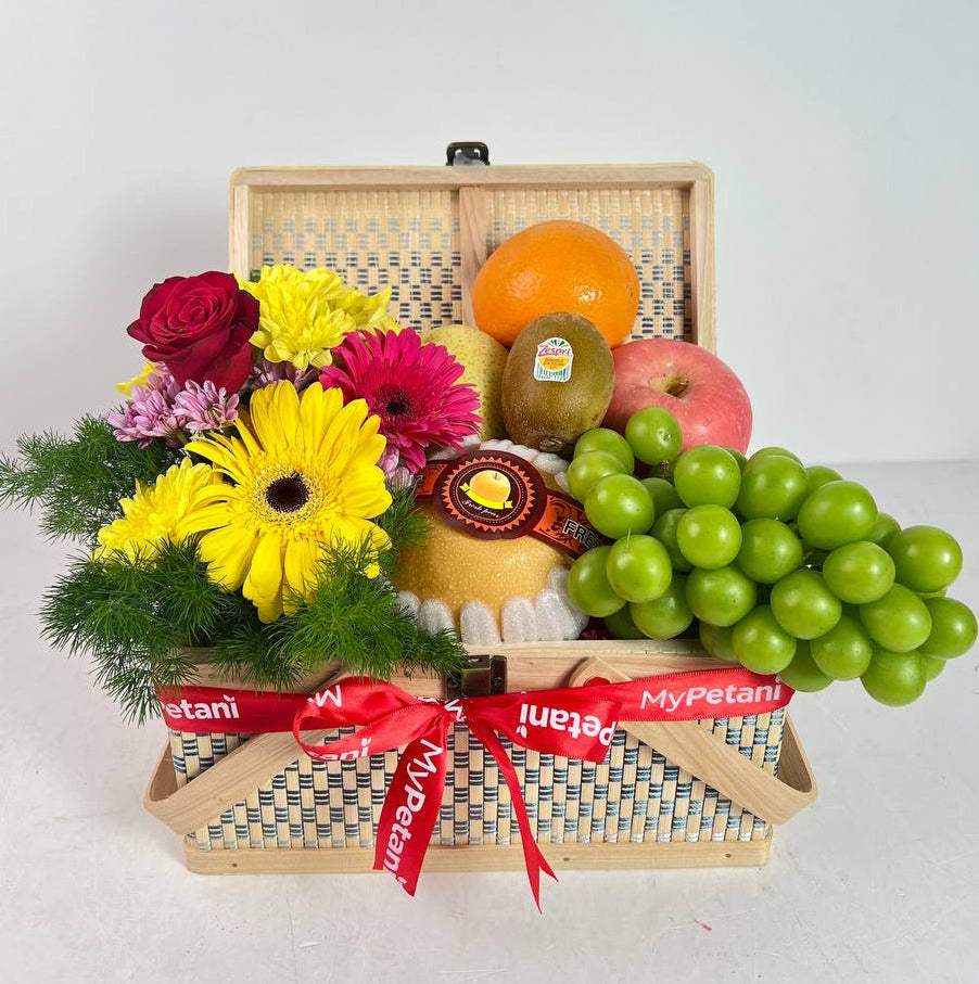 Gift basket with fruits, flowers, and a cheese wheel on a white background