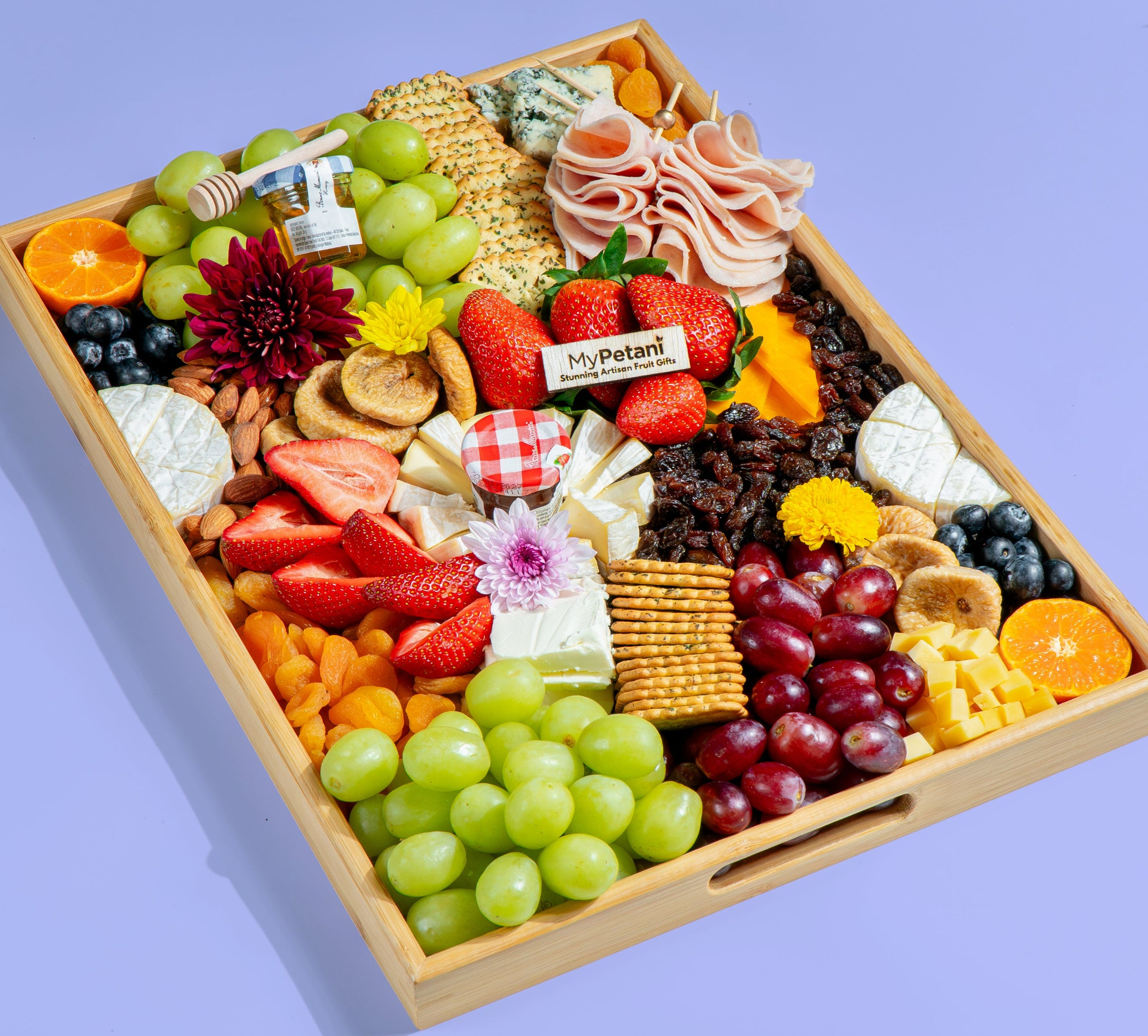 Assorted fruits, cheeses, and snacks on a wooden tray with a purple background