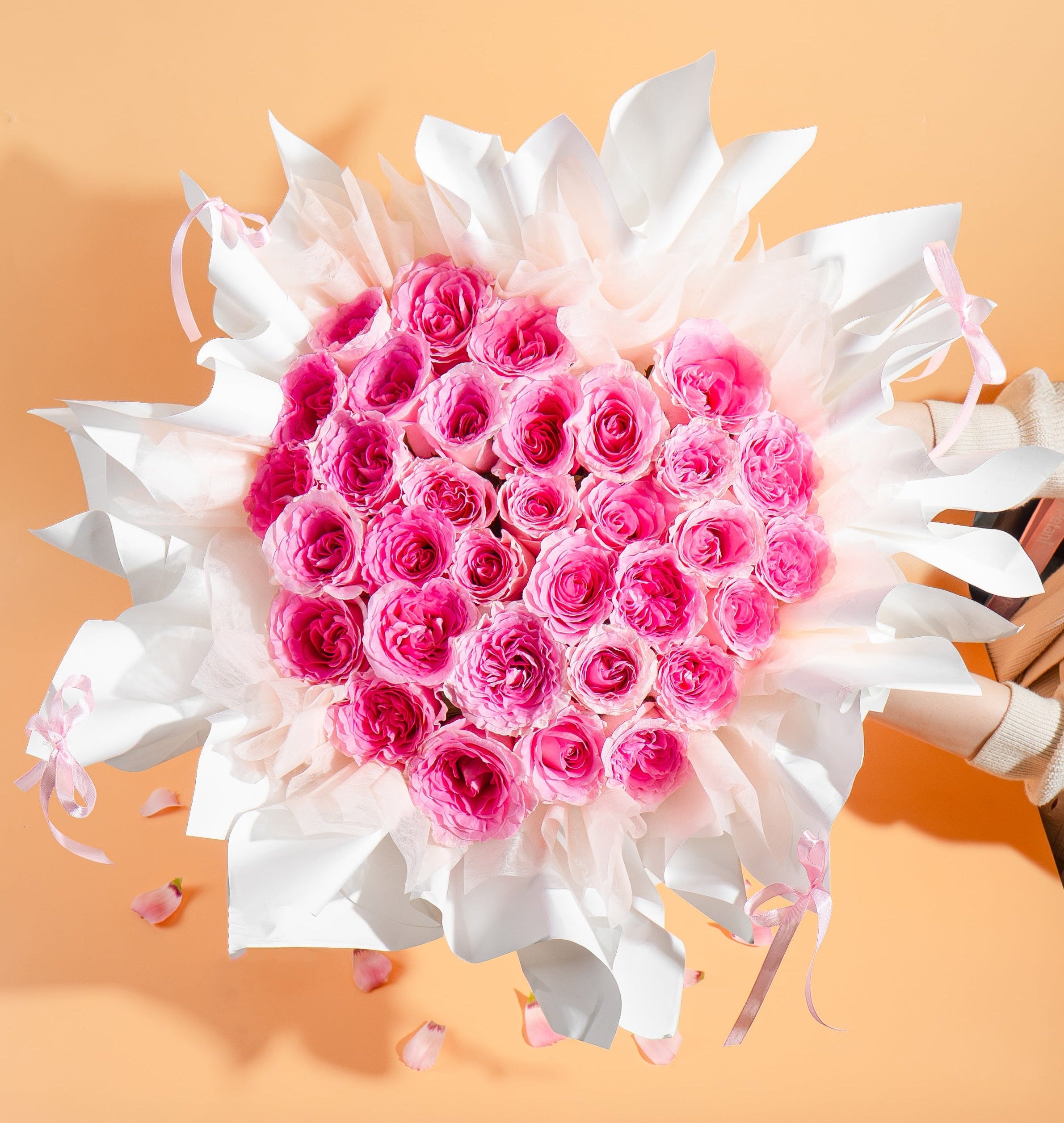 Heart-shaped arrangement of pink roses with white flowers on a peach background