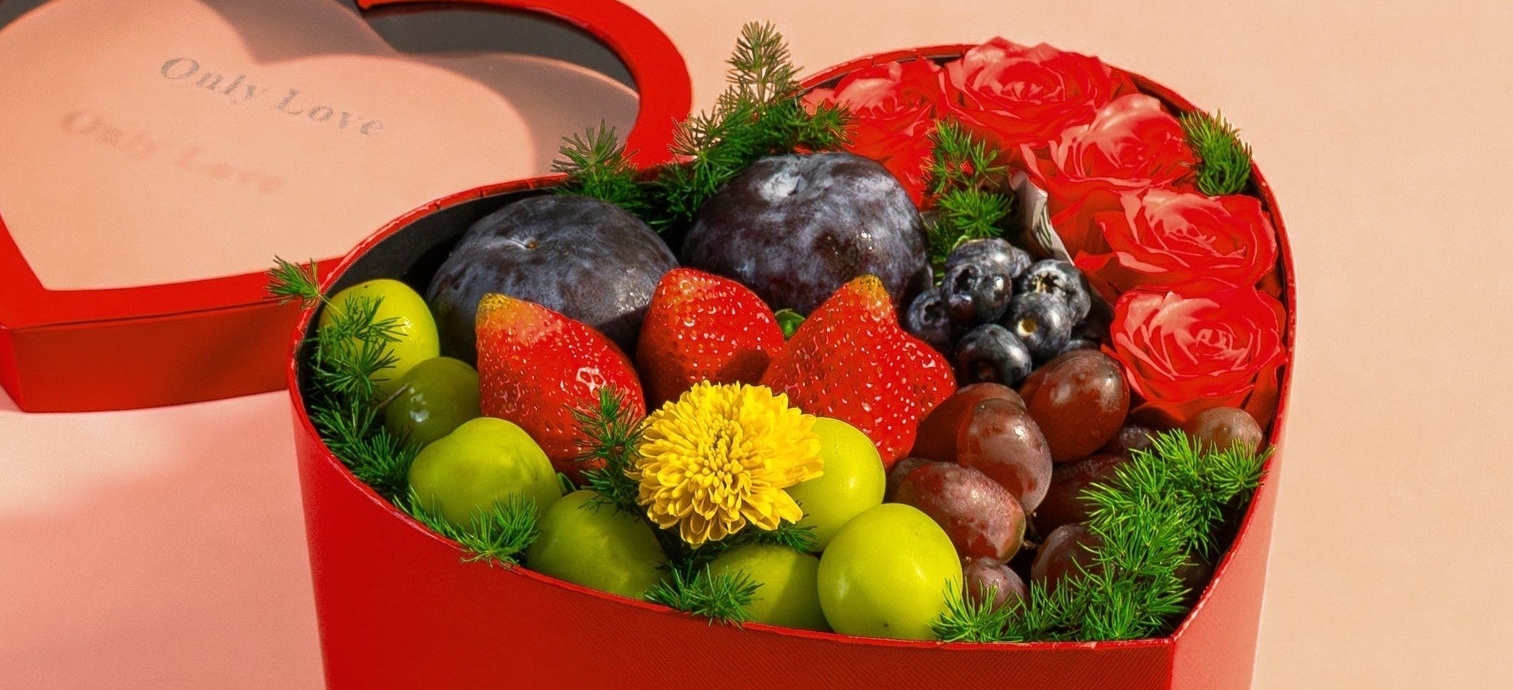 Heart-shaped box filled with fruits and flowers on a pink background