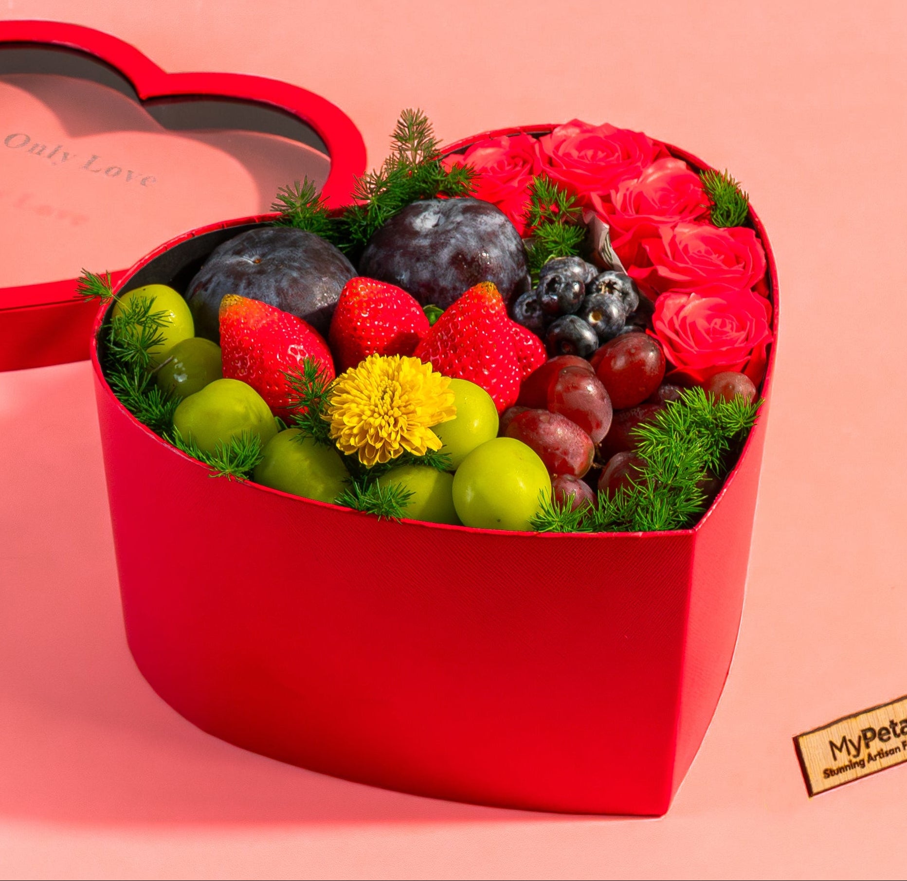 Heart-shaped red gift box filled with fruits and berries on a pink background