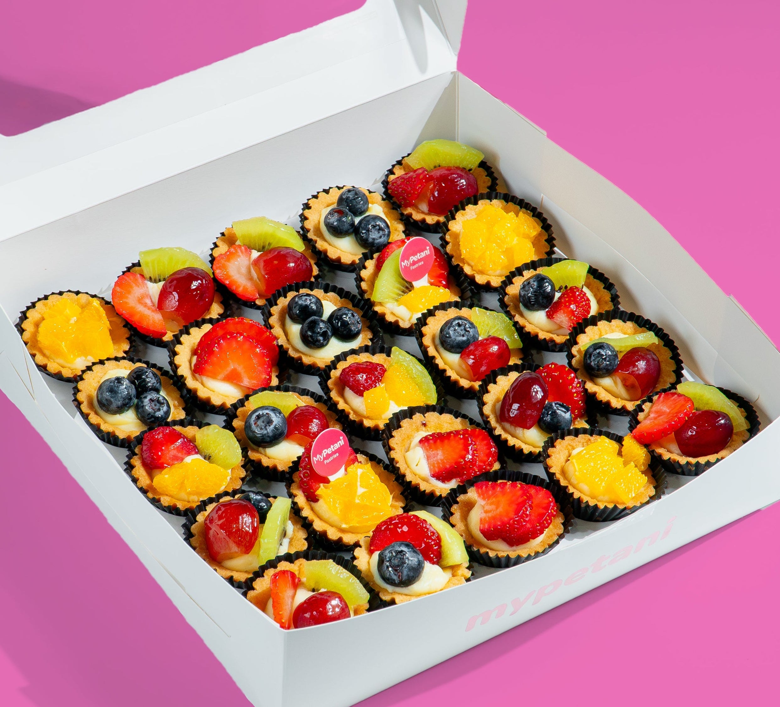 Box of colorful fruit tarts on a pink background