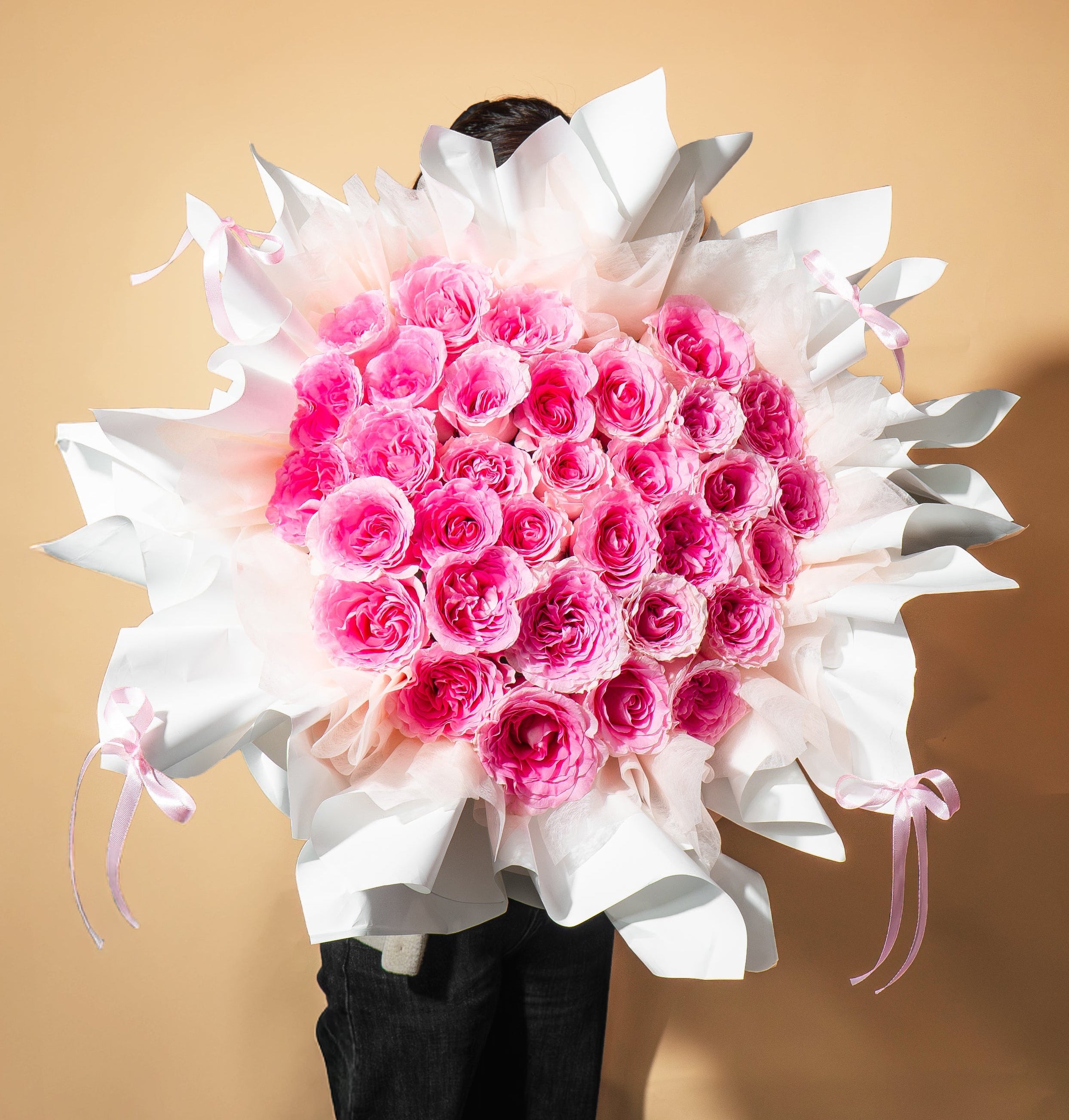 Bouquet of pink and white flowers held by a person against a beige background