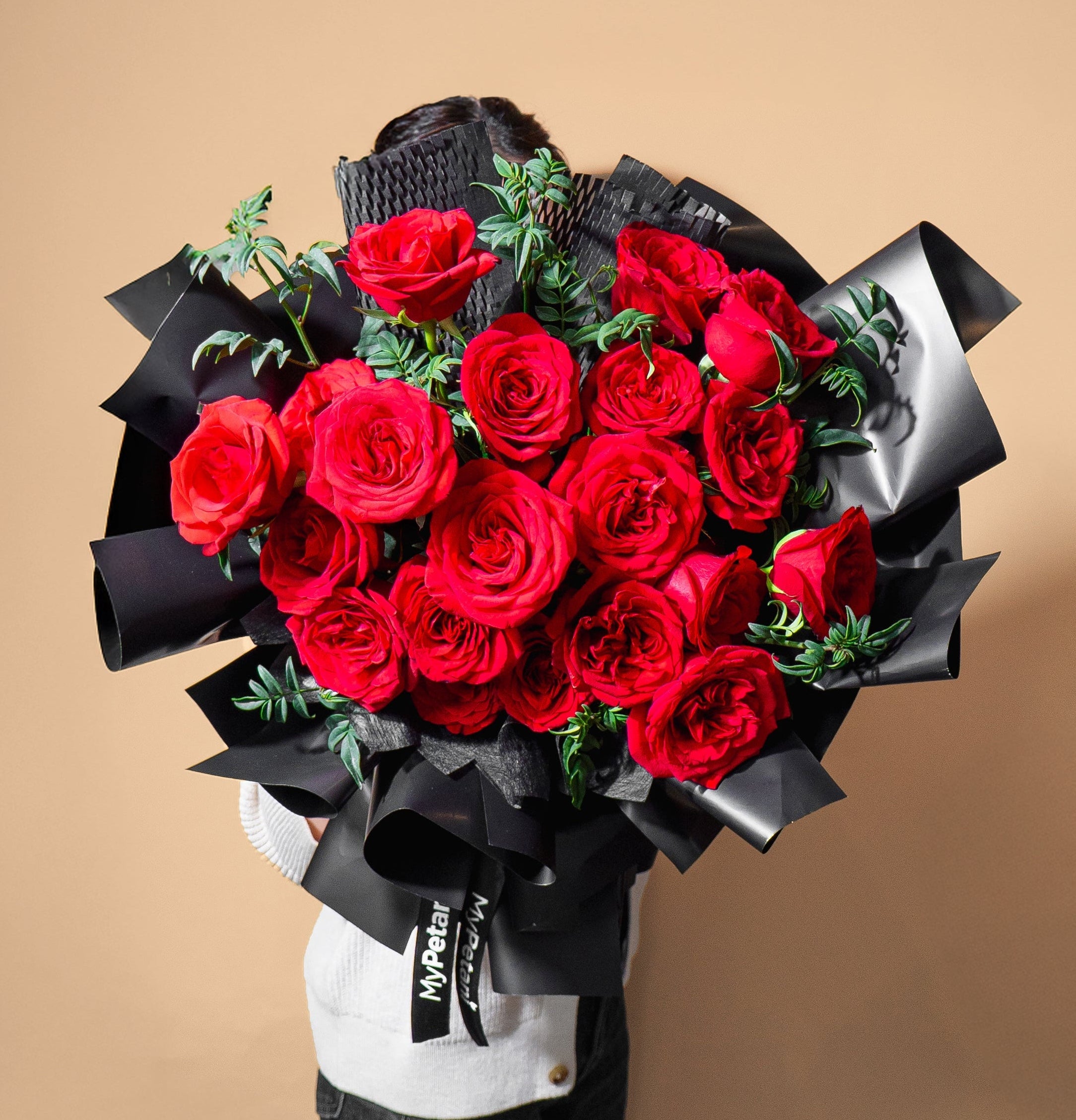 Bouquet of red roses wrapped in black paper held by a person against a beige background