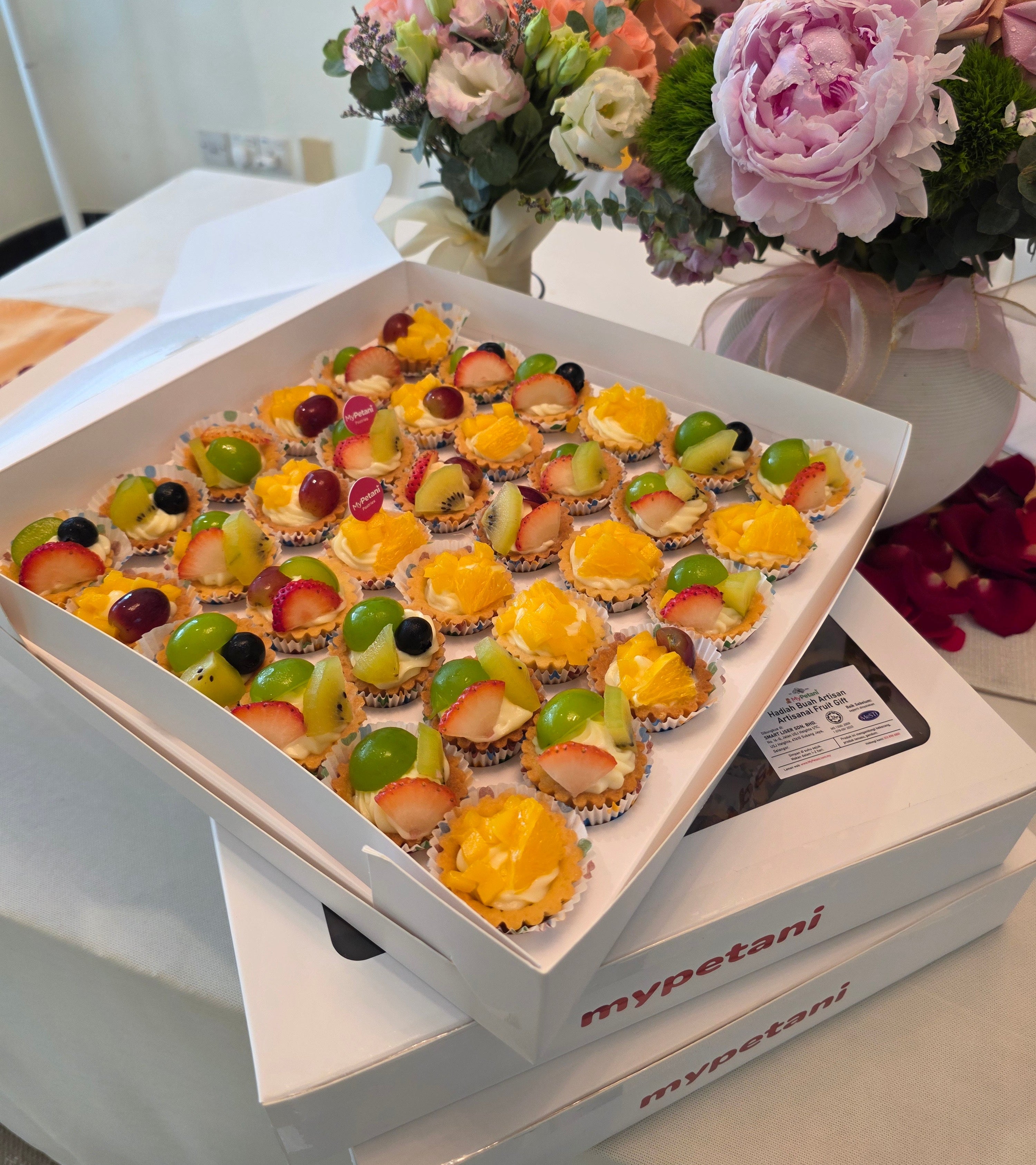 Box of small fruit tarts with flowers in the background